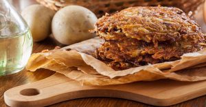 crispy homemade potato hash browns on parchment-lined wooden board with fresh potatoes and olive oil bottle nearby