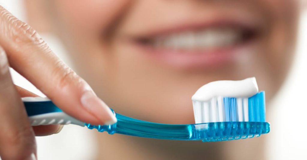 a person applying blue toothpaste from a tube onto a toothbrush for sensitive teeth care