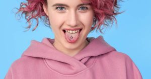 a person sticking out their tongue showing a tongue ring against a blue background