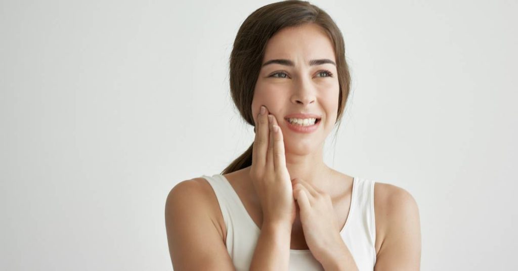 a smiling woman gently touching her cheek near her jaw, indicating potential toothache discomfort.