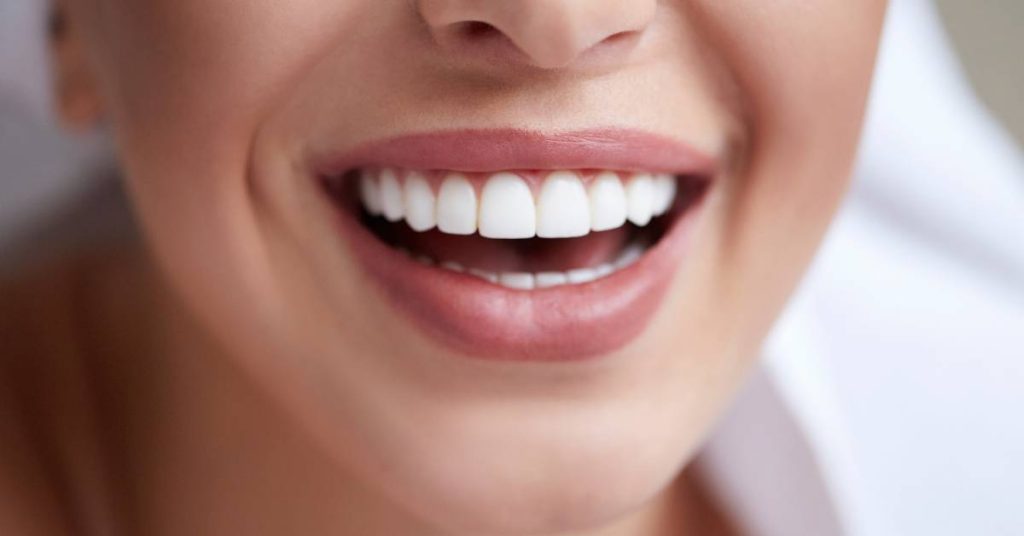 a close-up of a smiling person showing straight, bright white teeth and healthy gums