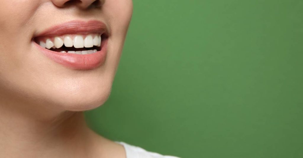 a smiling person showing healthy, clean teeth and gums against a green background